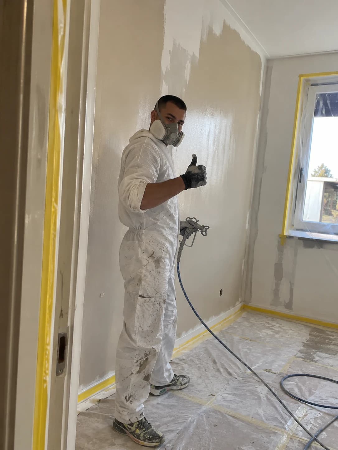 Schilder in witte overall met spuitmasker spuit een kamerwand in latex